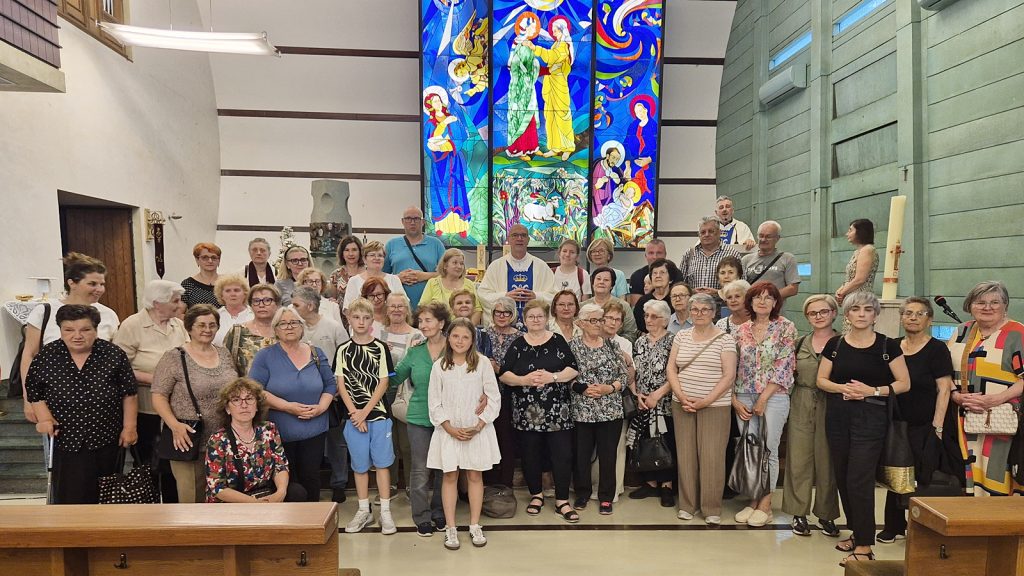 Diverse group of people standing together in a church nave with a vivid stained-glass window behind them.