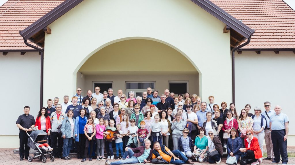 Large diverse group of people posing for a photo in front of a light building with an arched entrance.