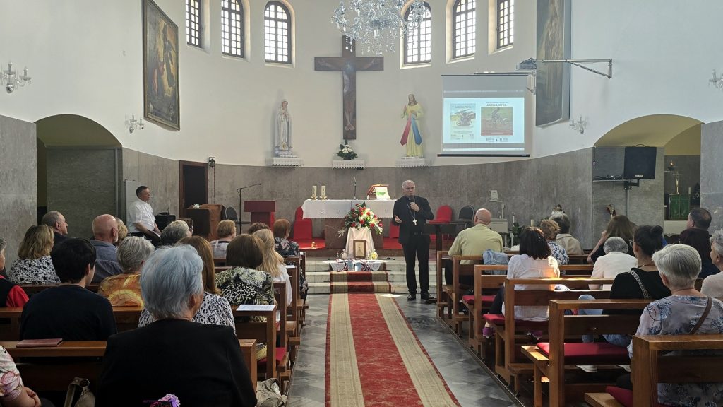 Clergy member delivering a sermon at the church altar, with a cross, statues, and projected slides nearby as the congregation listens.