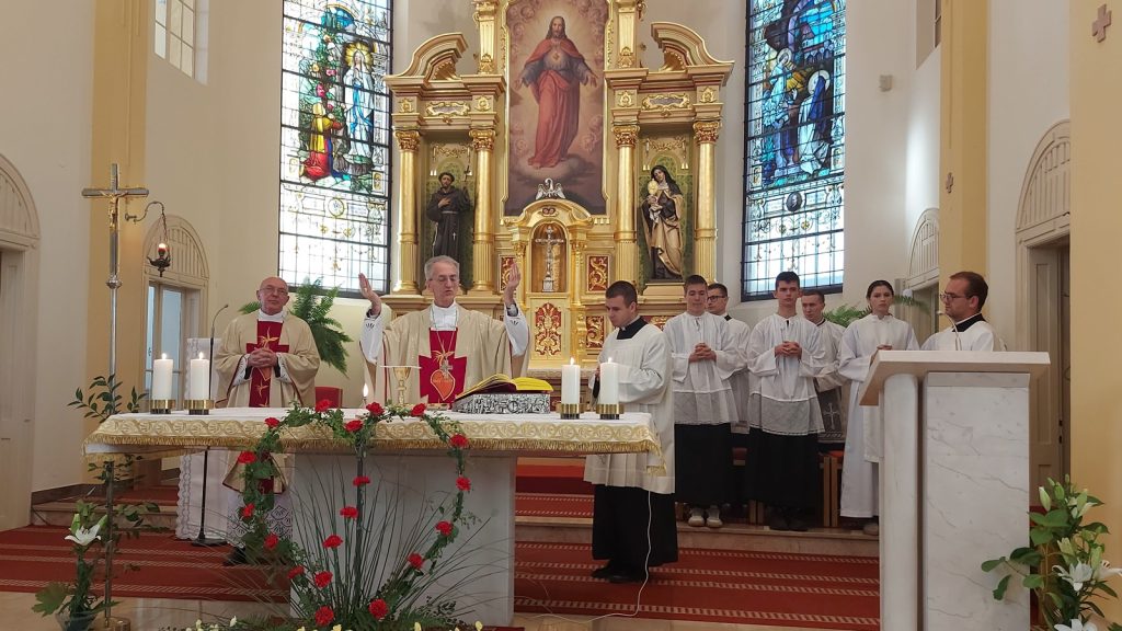 Priests at a gold-ornate altar during Mass, with altar servers in white robes beside them and stained-glass windows in the background
