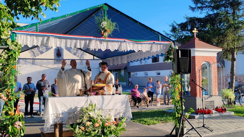 Outdoor Catholic Mass under a lace-decorated canopy; priests at an altar with worshippers watching nearby.