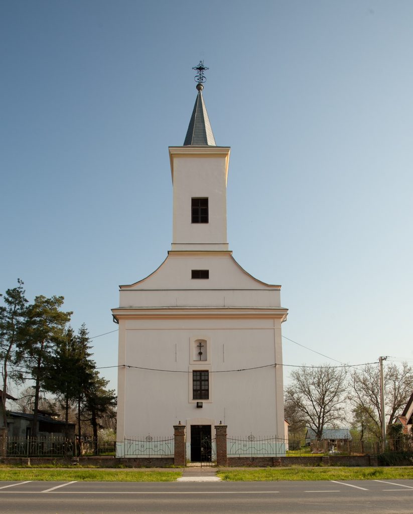 White church facade with tall steeple and decorative cross on top against clear blue sky