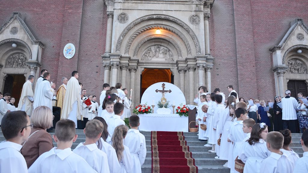 Children in white robes stand on both sides of a church altar during a religious ceremony outside a brick church.