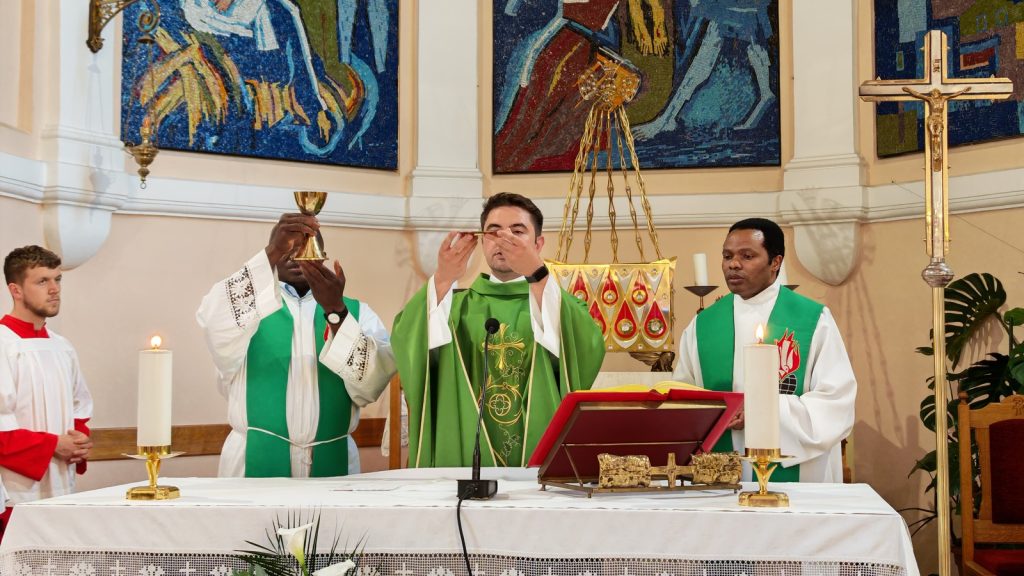 Catholic priests at an altar during Mass, central priest elevating communion while two assistants hold items nearby, ornate church setting in background