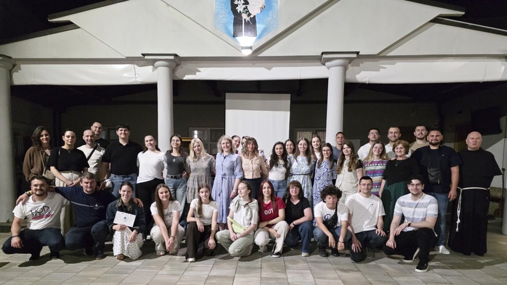 Large group of people posing for a photo outside a building with white columns at night.