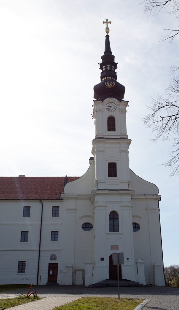 White church with a tall clock tower and onion-shaped dome topped by a cross, under a clear sky