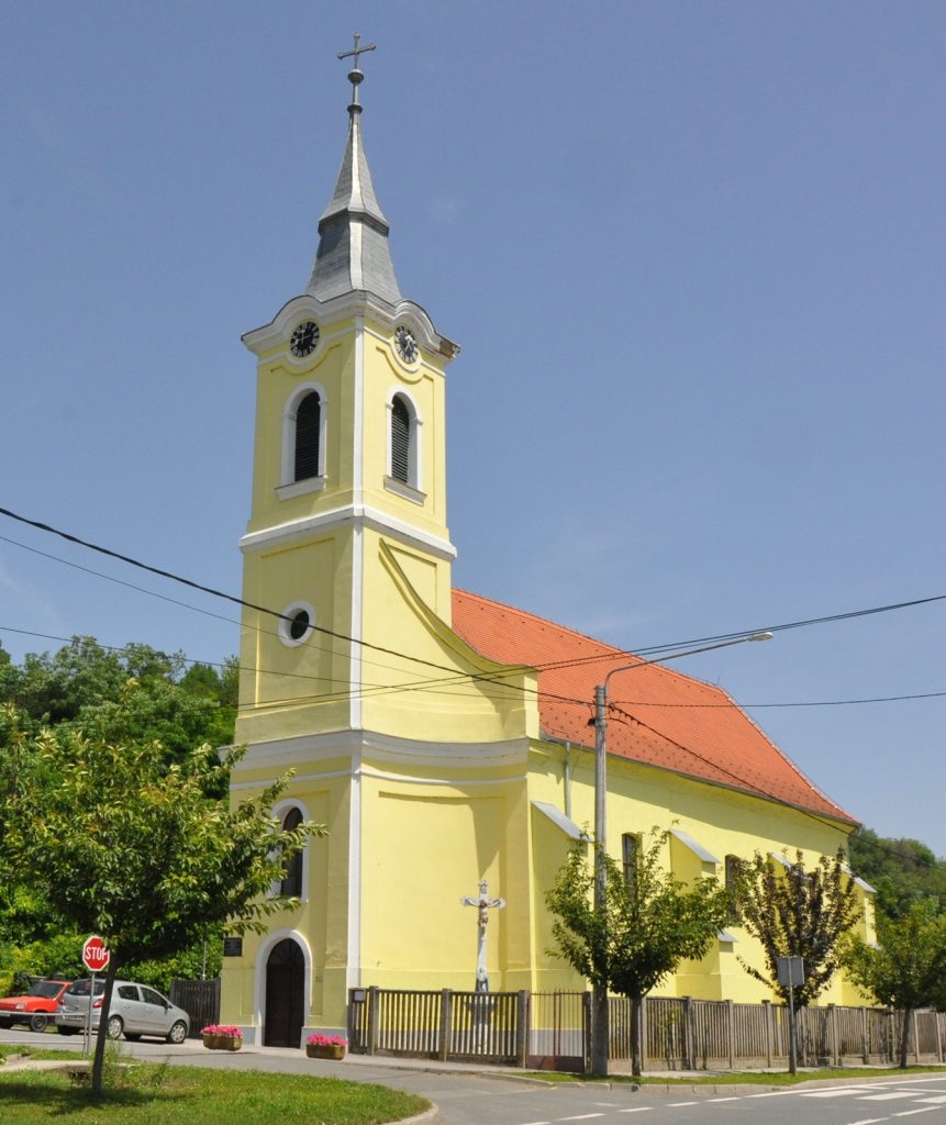 Yellow church with a tall steeple and clock tower against a clear blue sky.