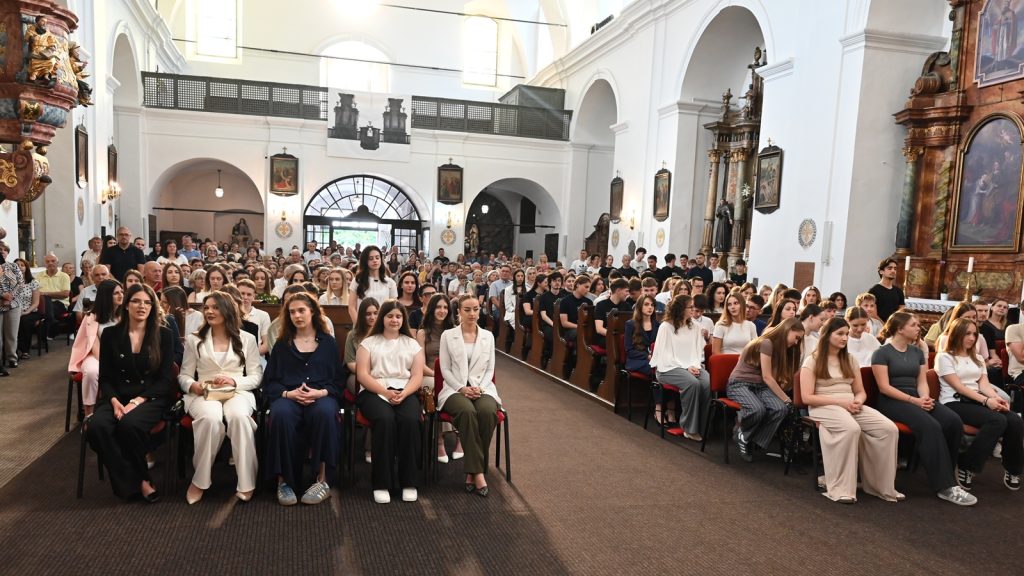 Large audience seated in a bright church nave for a ceremony, with ornate altarpiece on the right.