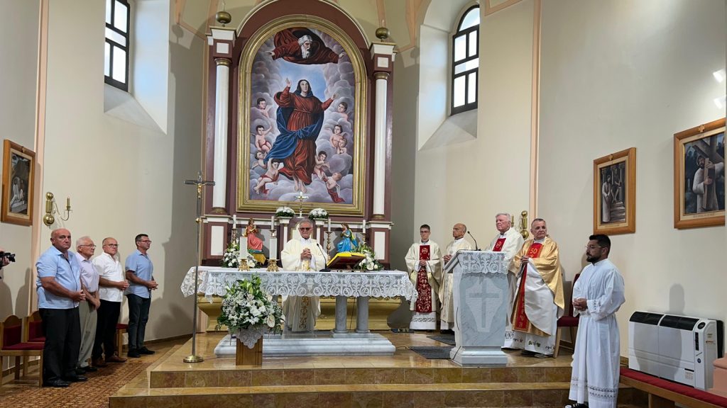 Catholic mass: priests at an ornate altar with a large religious painting behind them and worshippers on the left side of the church.