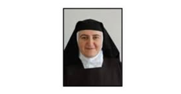 Portrait of a smiling nun in a black habit and white wimple facing the camera.