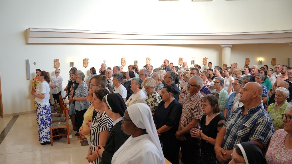 A crowded church gathering with people standing in prayer, including nuns in the foreground.