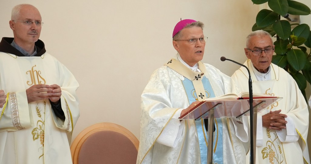 Three Catholic priests stand at a lectern during a service; the central bishop reads from an open book.