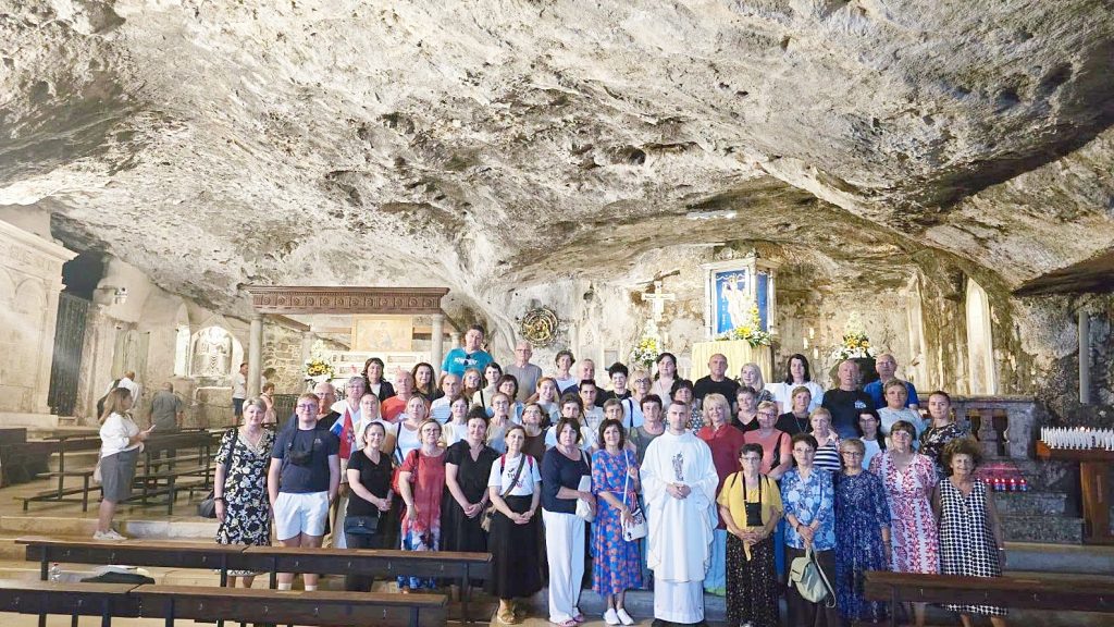 Large group of people posing inside a stone‑cave church with pews and an altar in the background.