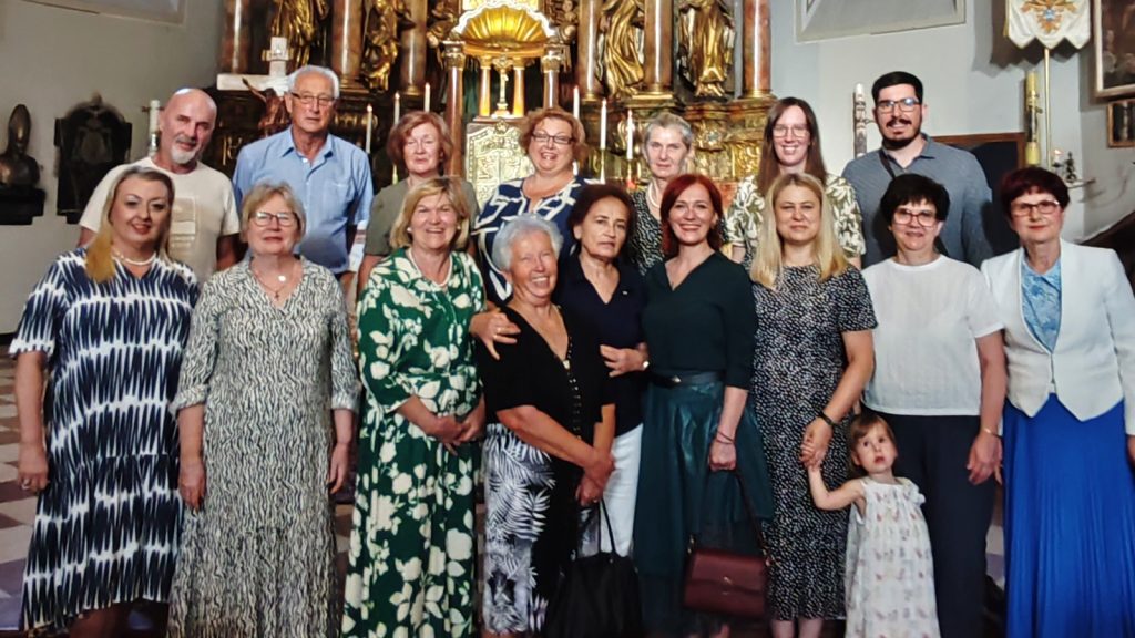 Group of adults (and a young girl) posing for a photo inside a church with a gilded altar behind them.